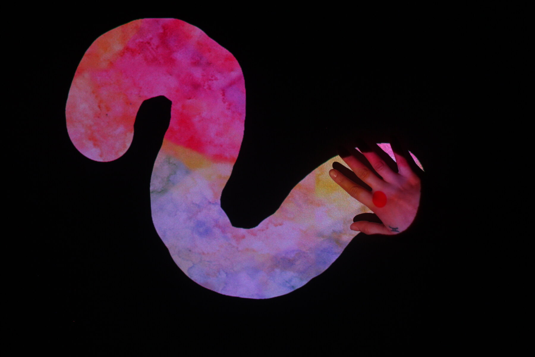 Hand interacting with colorful artwork projected onto a tabletop