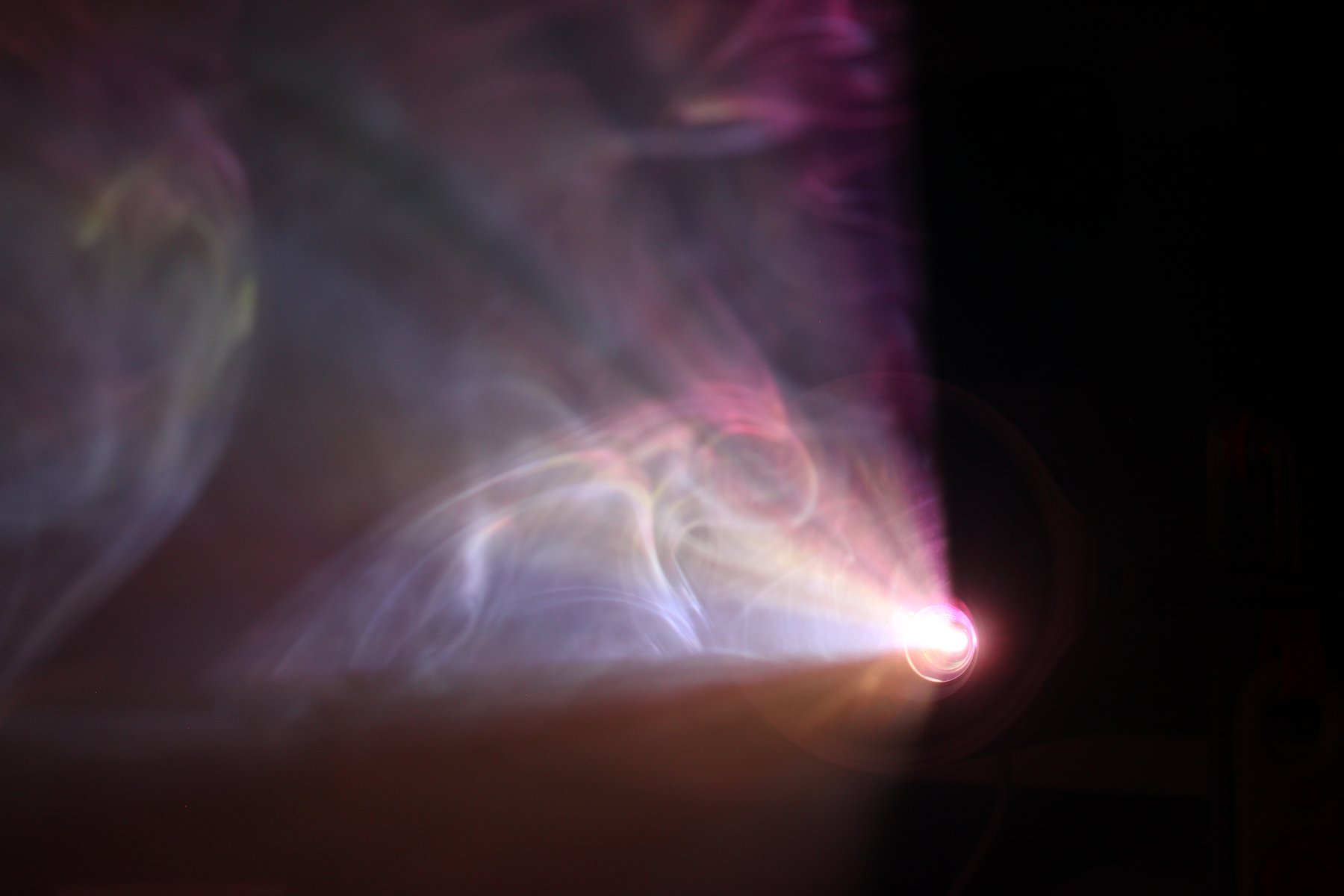 Violet projector beam cutting through layered colored smoke